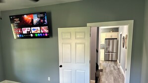 A room with a bed, a TV mounted on the wall, and a door leading to a kitchen area. - Newly Renovated House in Buffalo, Ky (Buffalo)