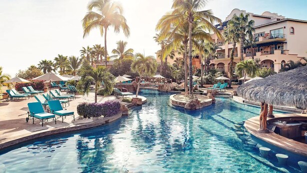Een zwembadgedeelte van een resort, met ligbedden, palmbomen en een jacuzzi.