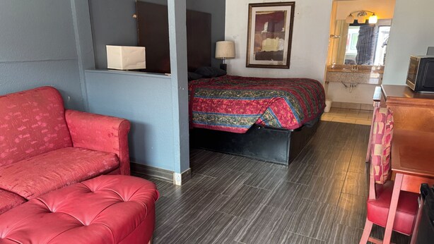 A room with a red sofa, a bed with a patterned bedspread, a wooden dresser, and a mirror. - Blue Way Inn & Suites Houston - Katy/Rosenberg Standard 1 King Bed NS (Rosenberg)
