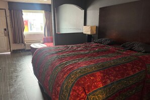 Ein Hotelzimmer mit einem großen Bett, einem roten Sessel, einem Fenster mit Vorhängen und einer Wandlampe.