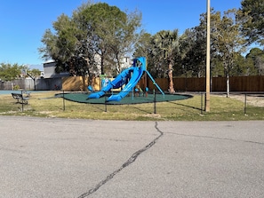 A playground with a blue slide and climbing structure, surrounded by a chain-link fence. - Seascape Villa 2A *Updated*Quiet villa*Beach access* (Miramar Beach)