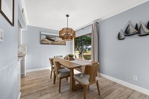 Un coin repas comprenant une table en bois, quatre chaises, un luminaire suspendu et une grande fenêtre avec des rideaux.