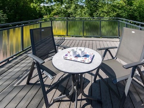 Eine Terrasse im Freien mit einem runden Tisch, zwei Stühlen und einer Ablage mit Tassen und Untertellern.