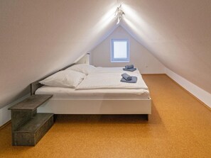 Ein Einzelbett mit Kopfstütze, einem kleinen Fenster und einer hölzernen Sitzbank.