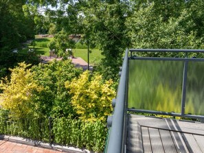 Une vue depuis un balcon donnant sur un jardin, avec une terrasse en bois et une rambarde en métal.