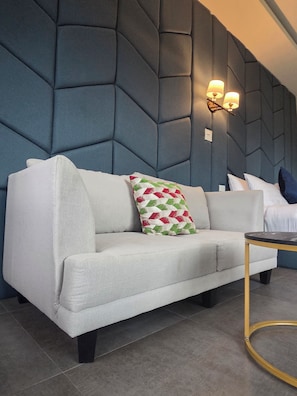 A modern living room with a sofa, a patterned throw pillow, a small round table, and a wall-mounted light fixture. - KIREERIVER (Thong Pha Phum)