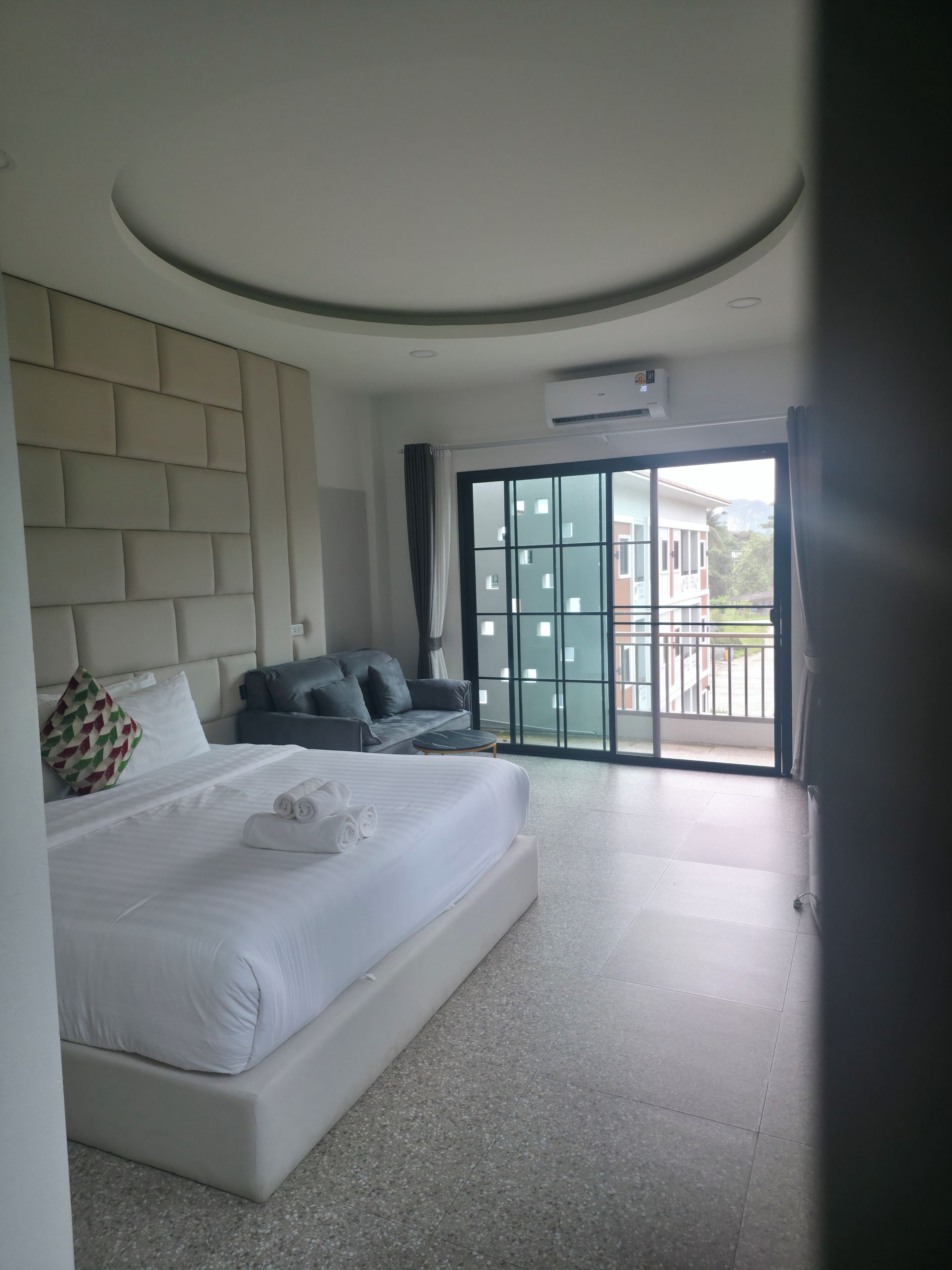 Ein modernes Hotelzimmer mit einem großen Bett, einer Couch, einem kleinen Tisch und Blick auf ein Gebäude durch eine Glastür.
