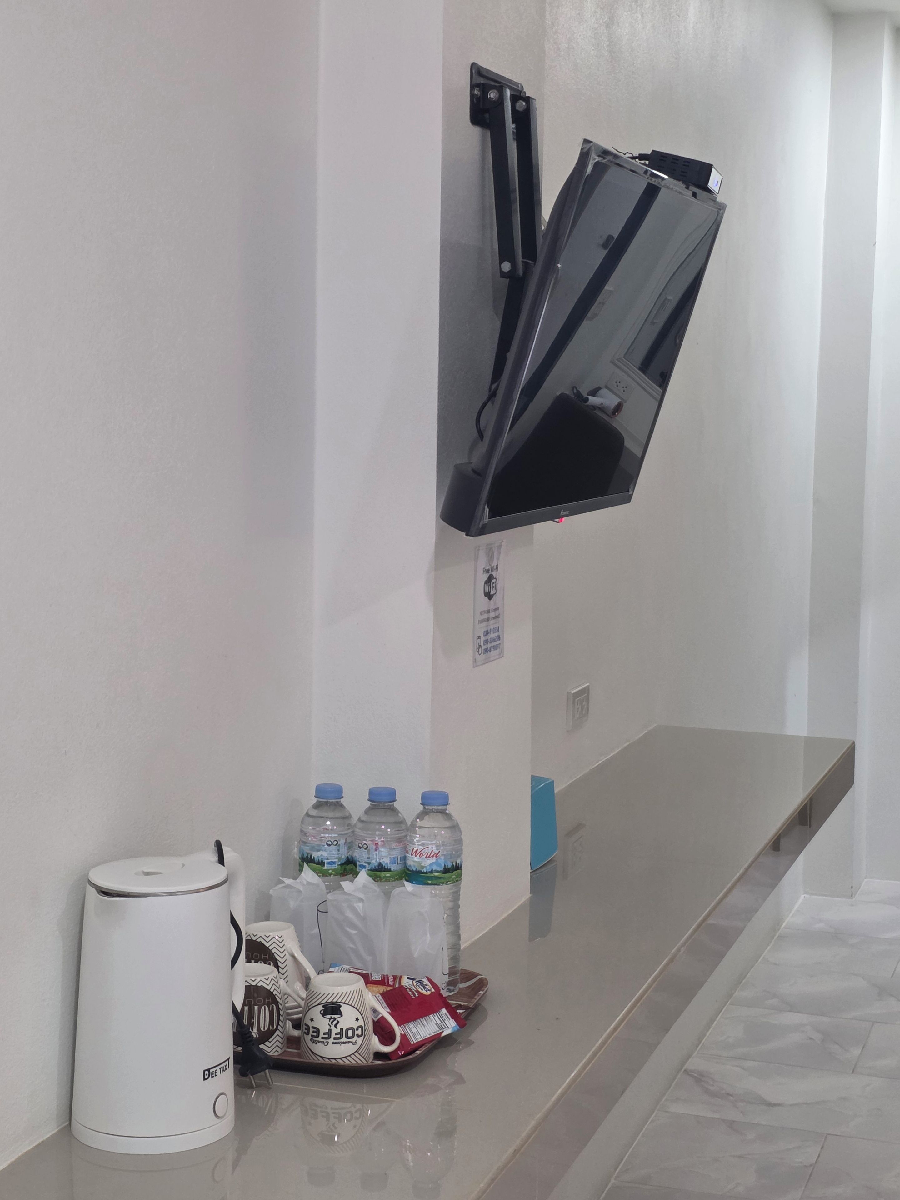 A hotel room with a flat-screen TV mounted on the wall, a coffee maker, and a tray with bottled water and coffee mugs.