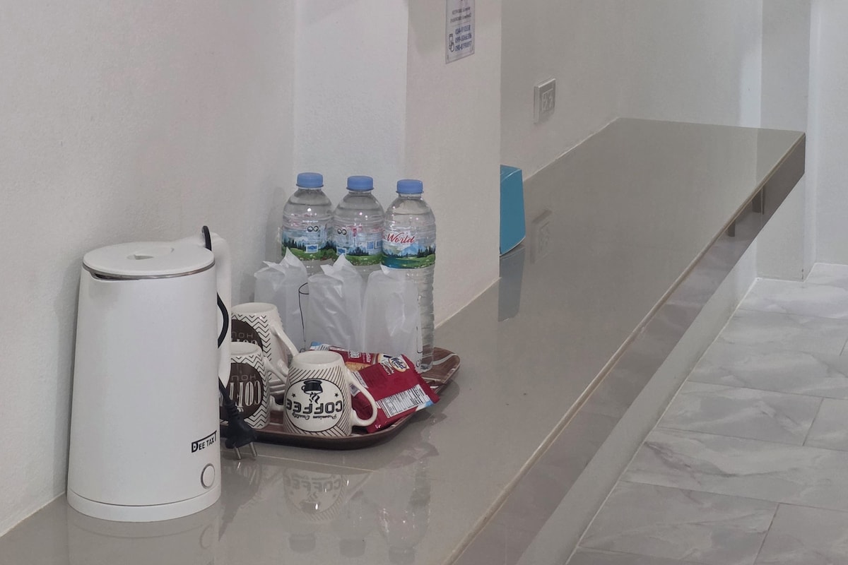 Habitación de hotel con televisor de pantalla plana montado en la pared, cafetera y bandeja con agua embotellada y tazas de café.