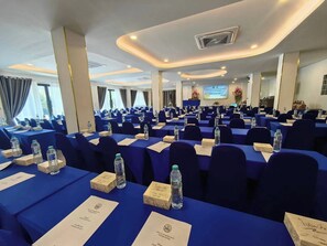 A conference room with rows of tables, chairs, nameplates, water bottles, and snack boxes.
