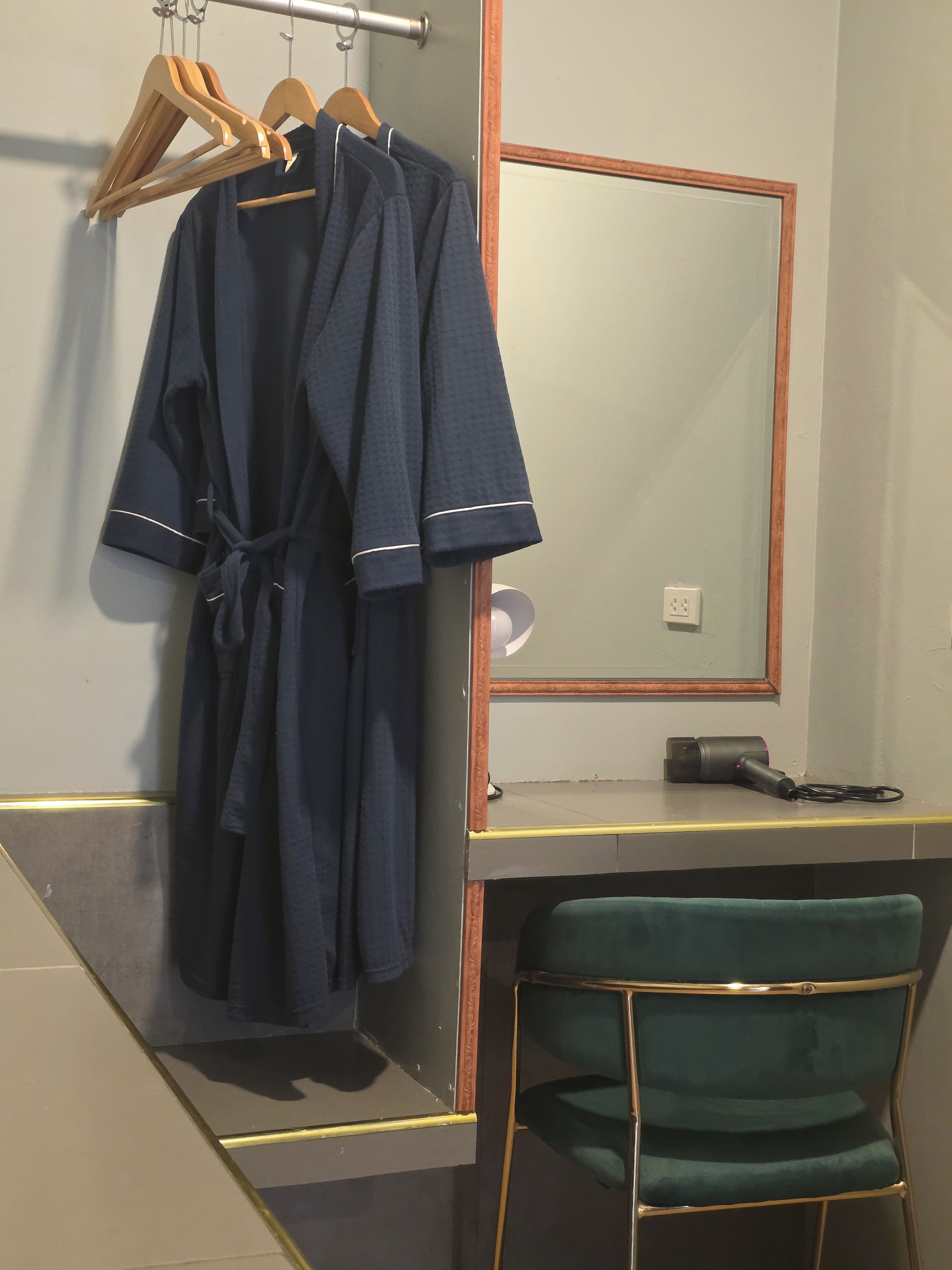 A bathroom with a mirror, a robe hanging on a rack, a hairdryer on the counter, and a green chair.