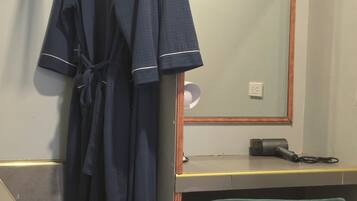 A bathroom with a mirror, a robe hanging on a rack, a hairdryer on the counter, and a green chair.