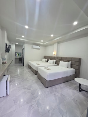 A hotel room with three beds, a small table, a TV, and an air conditioning unit. - KIREERIVER (Thong Pha Phum)