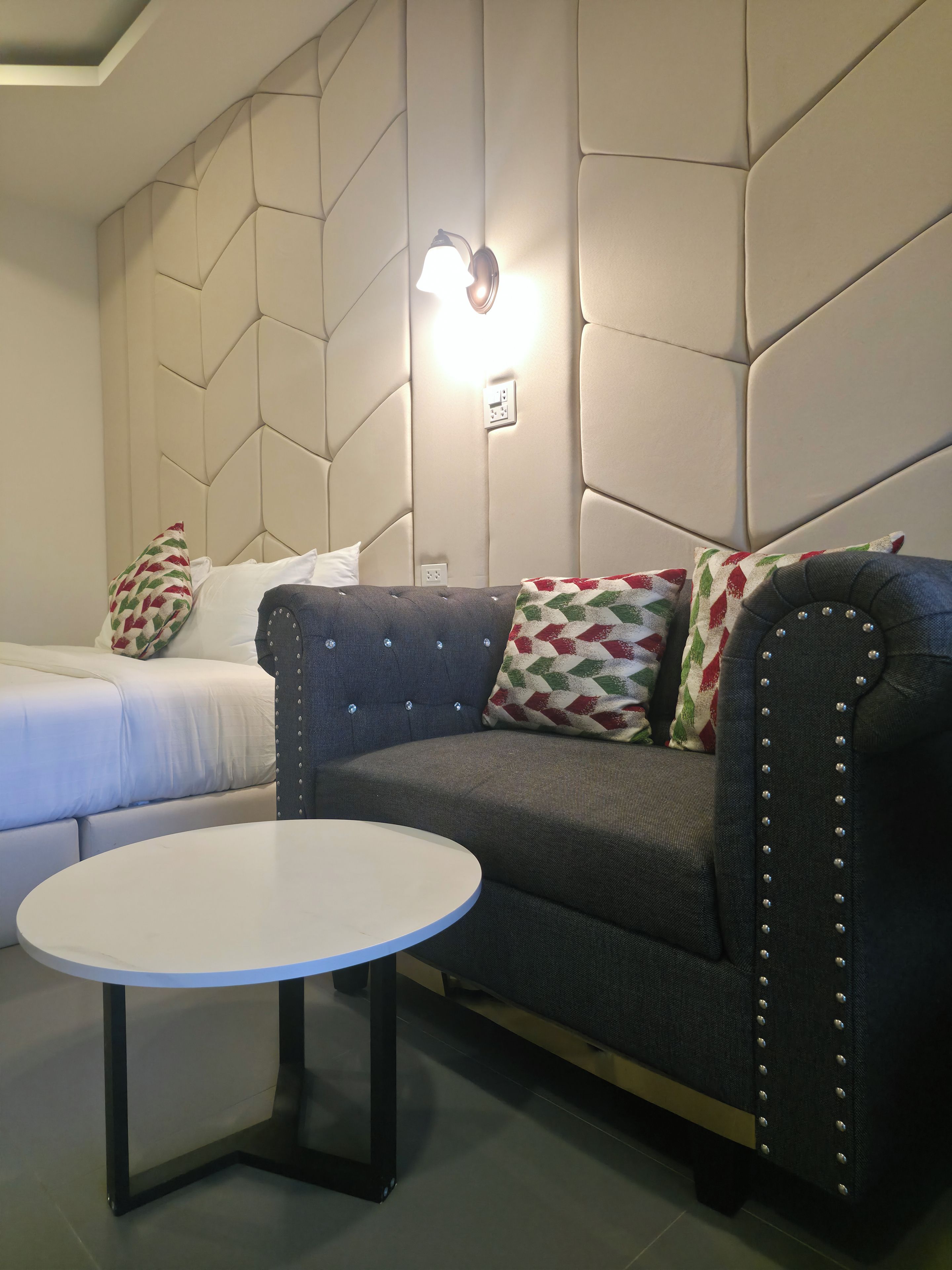 Une chambre moderne avec un canapé, une petite table ronde et un lit agrémenté d’oreillers à motifs.