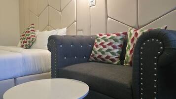 Une chambre moderne avec un canapé, une petite table ronde et un lit agrémenté d’oreillers à motifs.