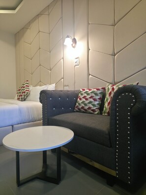 A modern room with a sofa, a small round table, and a bed with patterned pillows.