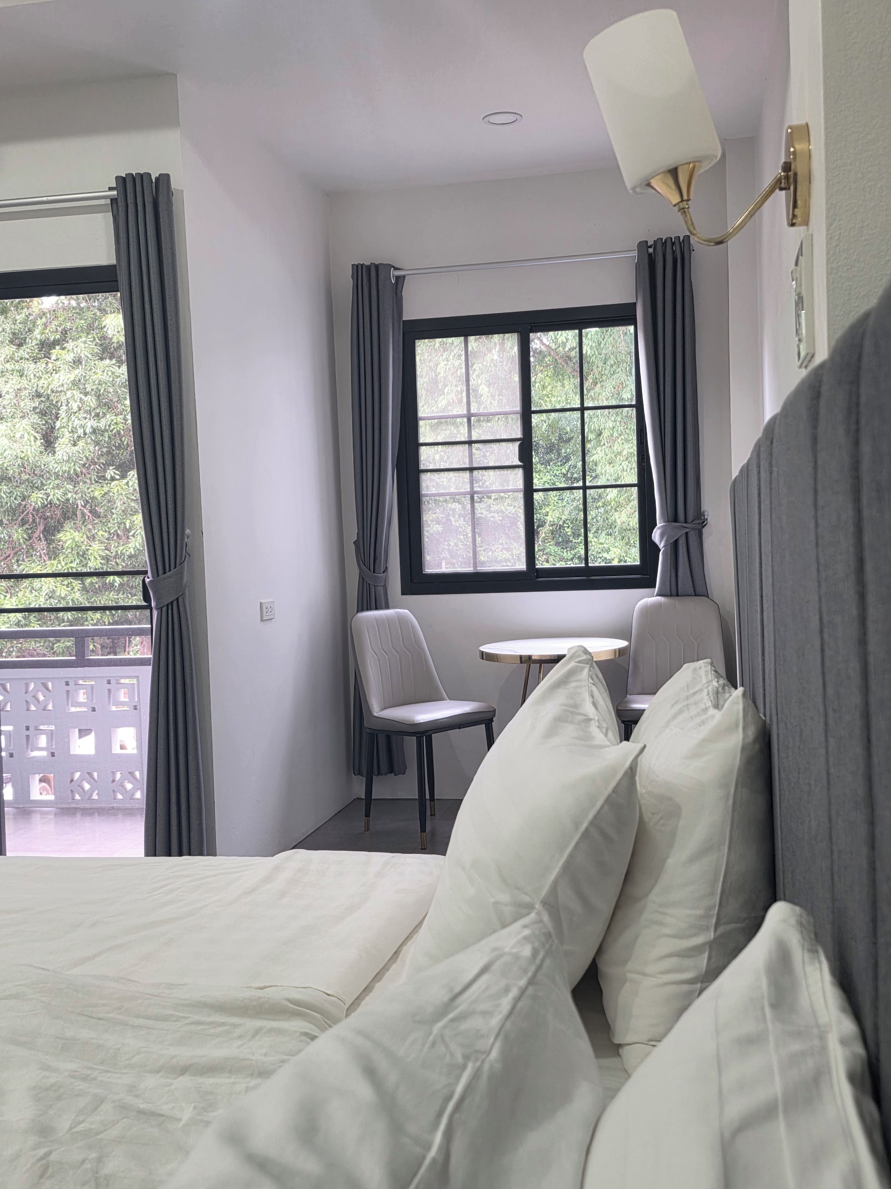 A hotel room with a bed, a small table, two chairs, and a window with curtains.