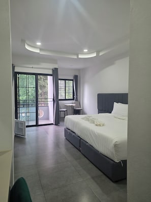 Moderni hotellihuone, jossa on suuri sänky, työpöytä ja näkymä lasiovesta.