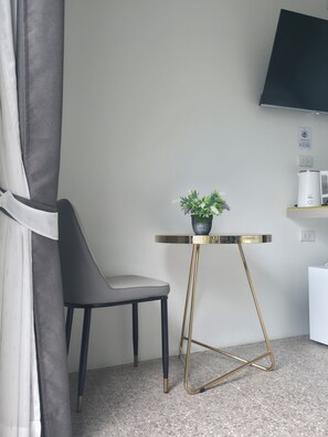 A modern room with a grey chair, a small table with a plant, a white coffee maker, and a flat-screen TV mounted on the wall.