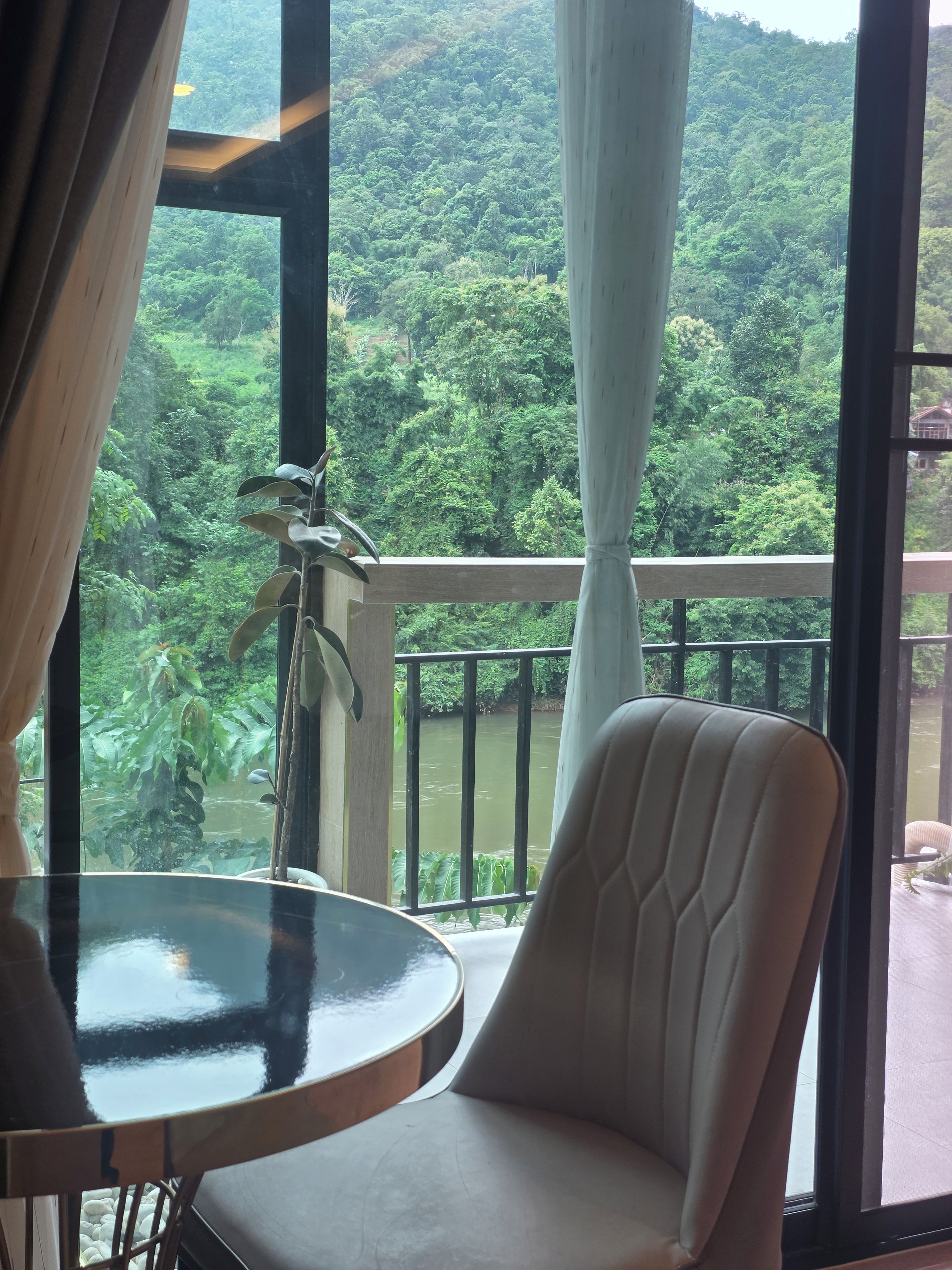 Habitación con vista a un bosque frondoso y un río. Hay una silla y una mesita.