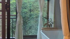 Un baño con bañera, una ventana con cortinas y vistas a zona boscosa.