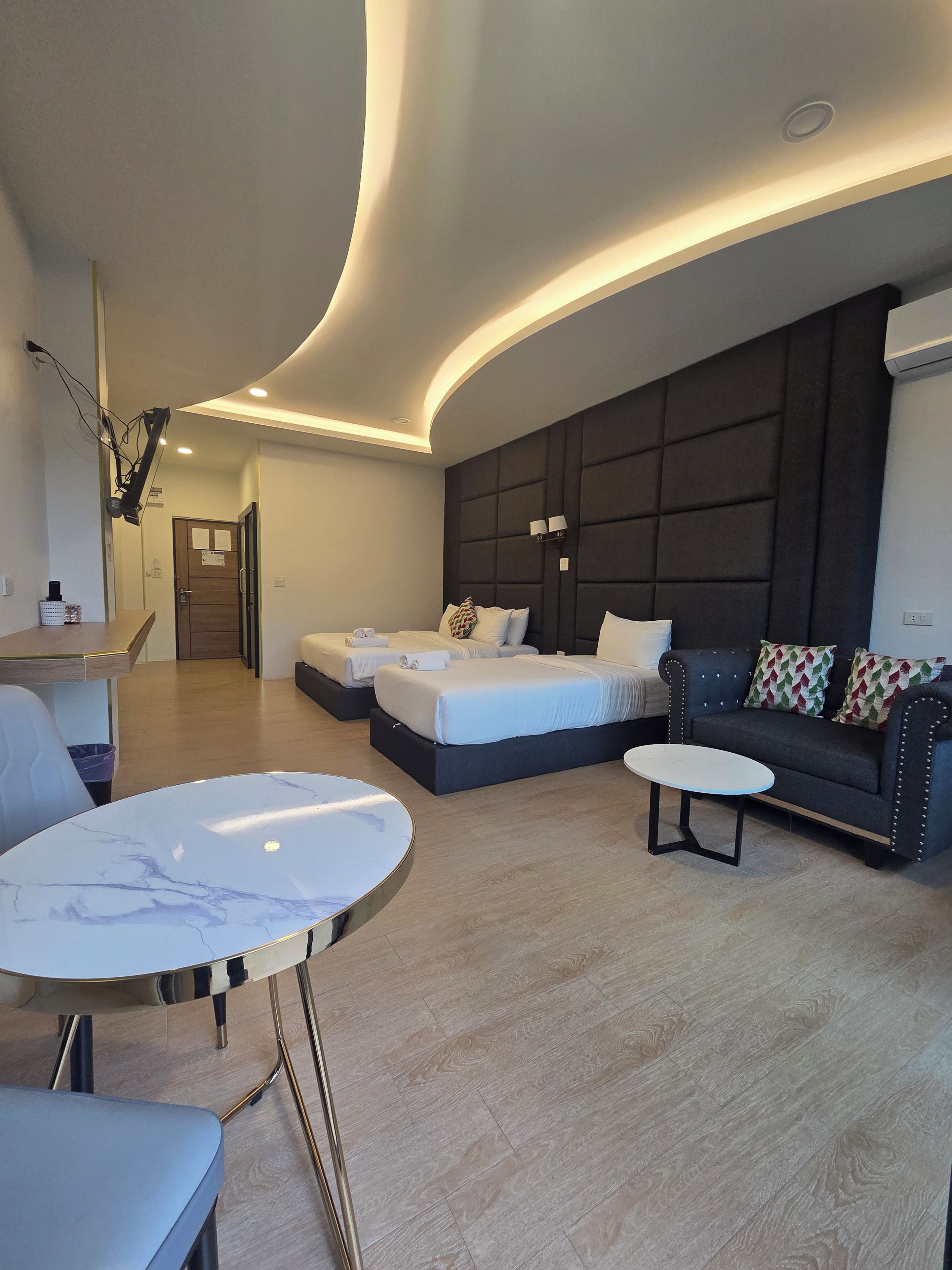Habitació d'hotel moderna amb sostre corbat, un sofà, un llit amb dos coixins, una taula rodona petita i una cadira.