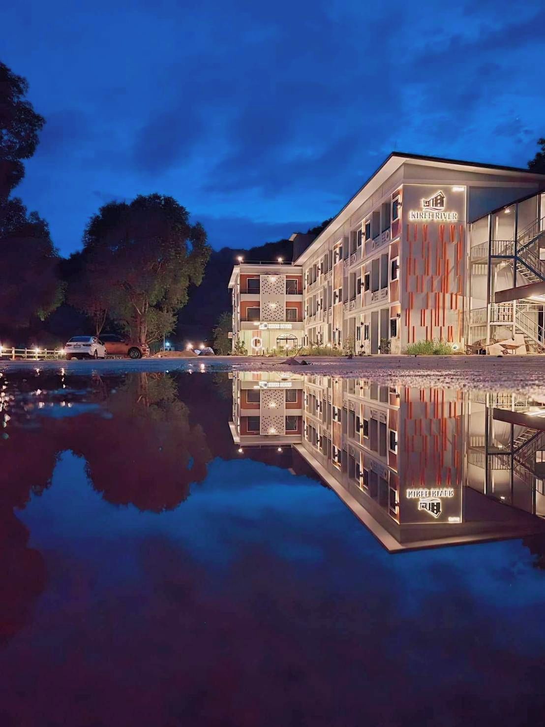 Un hotel de varios pisos con una piscina reflectante al frente.