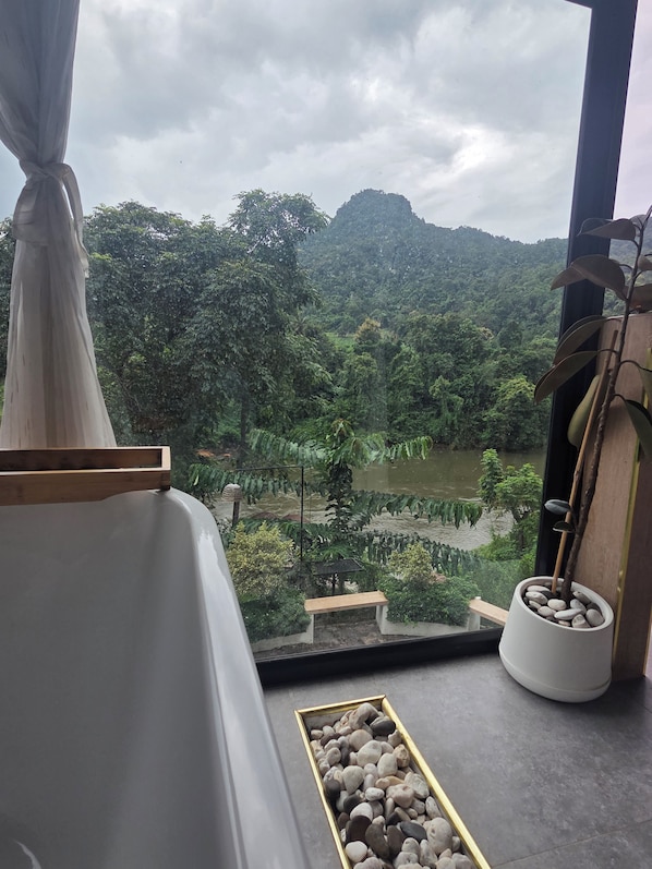 A room with a view of a lush landscape, a bed, a small table, and a potted plant. - KIREERIVER (Thong Pha Phum)