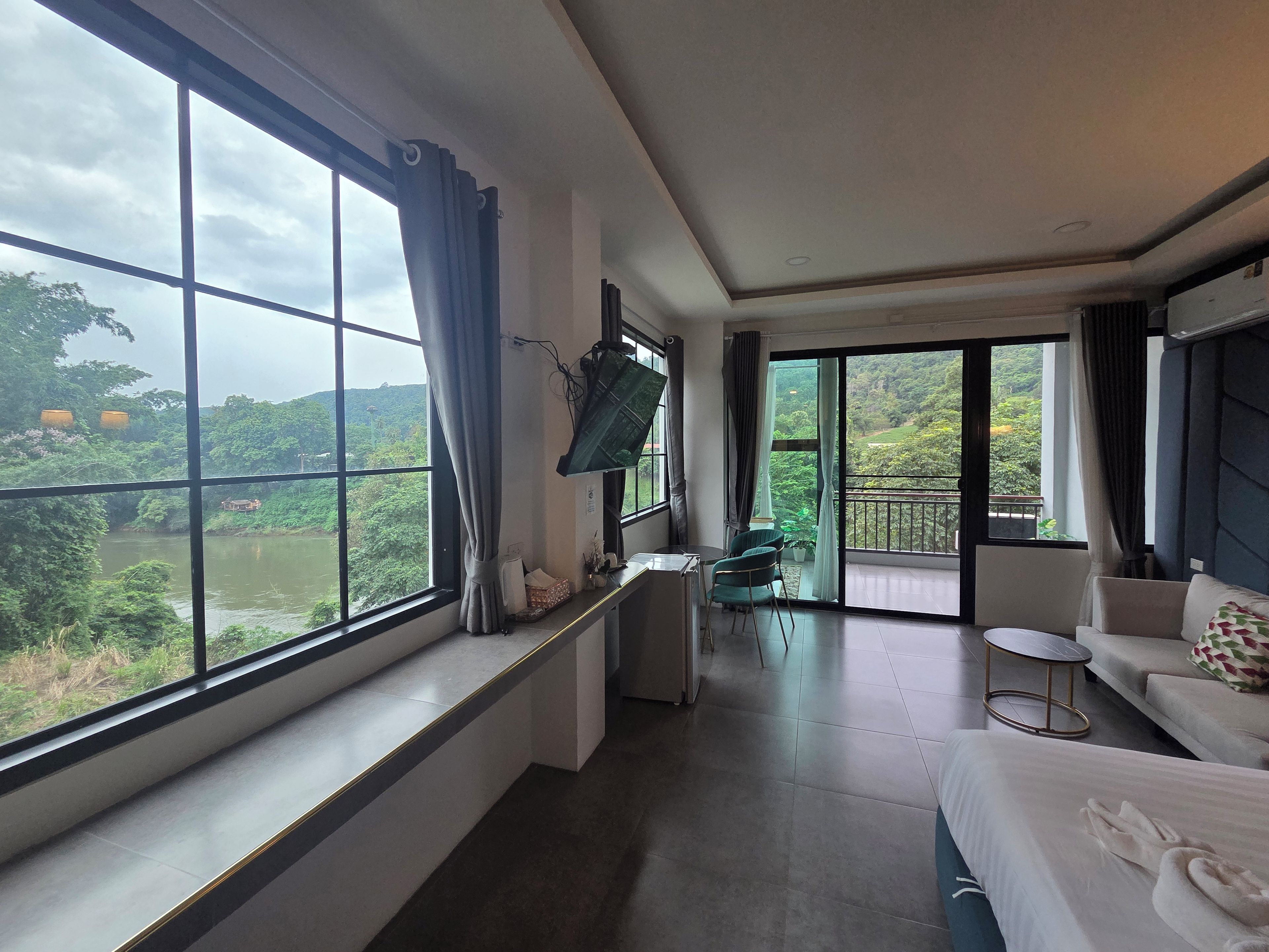 A hotel room with a large window, a flat-screen TV, a sofa, and a bed.