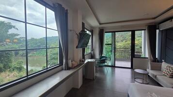A hotel room with a large window, a flat-screen TV, a sofa, and a bed.