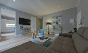 A modern living room with a large sofa, a coffee table, and a TV. There is a kitchen in the background with a flat-screen TV mounted above the counter. - CENTRAL FLORENCE RETREAT NEAR PONTE VECCHIO & UFFIZI (Firenze)