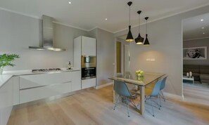 A modern kitchen with white cabinetry, a gas stove, and an oven. There is a dining area with a glass table and blue chairs. - CENTRAL FLORENCE RETREAT NEAR PONTE VECCHIO & UFFIZI (Firenze)