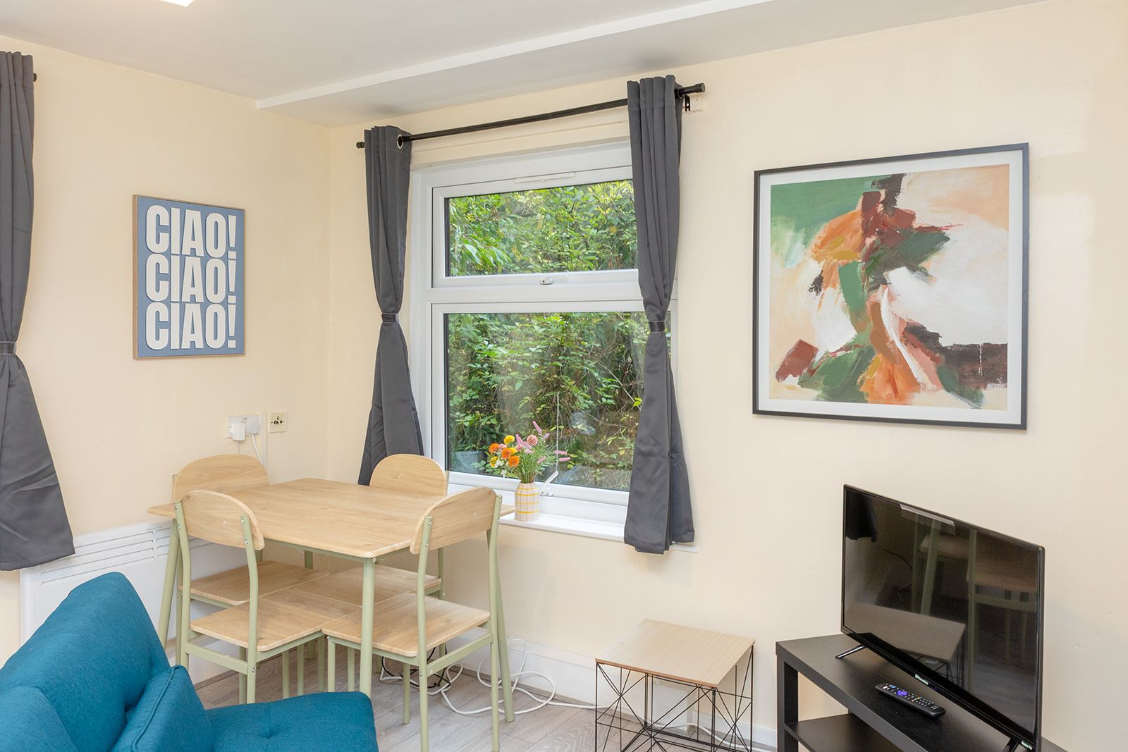 A room with a dining table, chairs, a TV, and artwork on the walls.