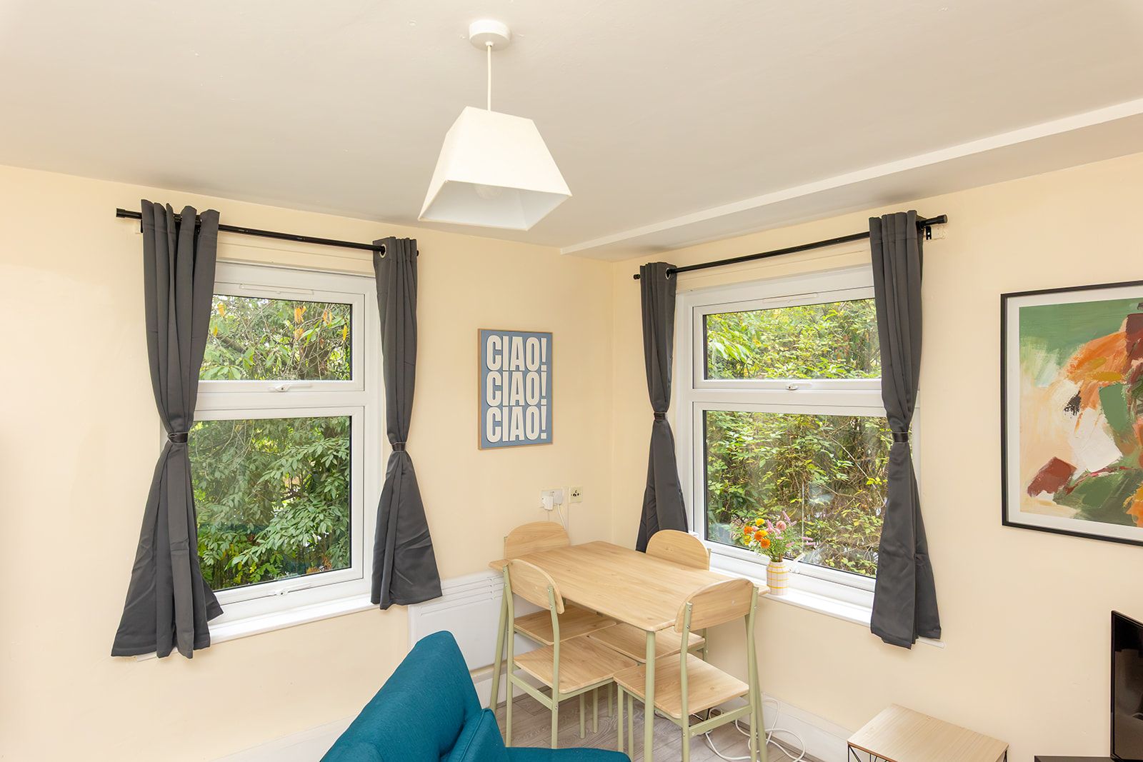 A room with two windows, a table with chairs, a sofa, a lamp, and a framed picture on the wall.