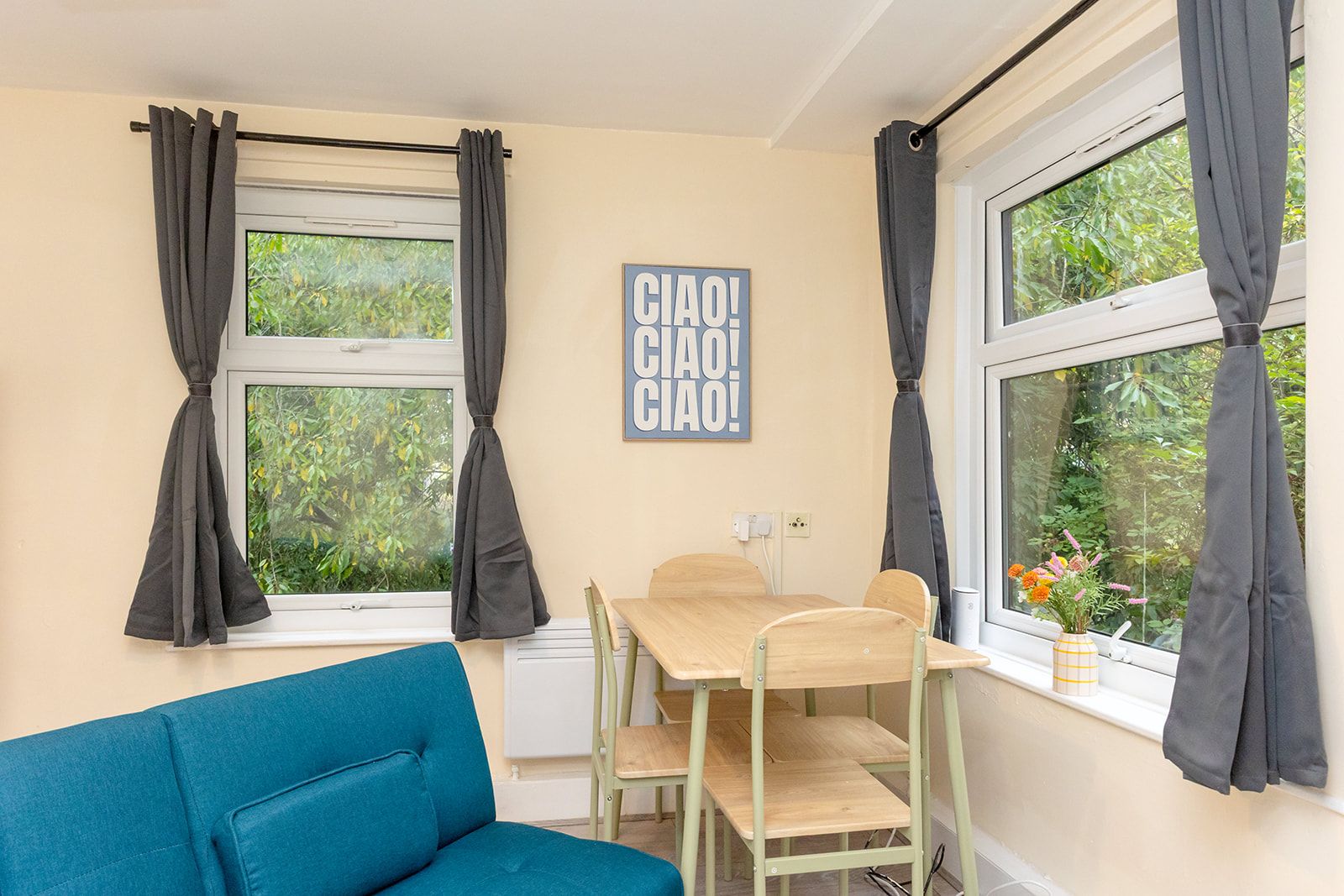 Ein Zimmer mit einem blauen Sofa, einem Holztisch mit Stühlen, einem Fenster mit Vorhängen und einem an der Wand befestigten Schild.