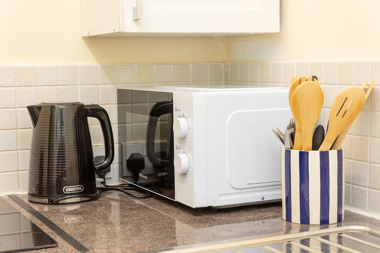 Uma cozinha com cafeteira, micro-ondas e suporte para utensílios no balcão.