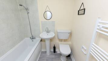 A compact bathroom with a bathtub, sink, toilet, and a shower.