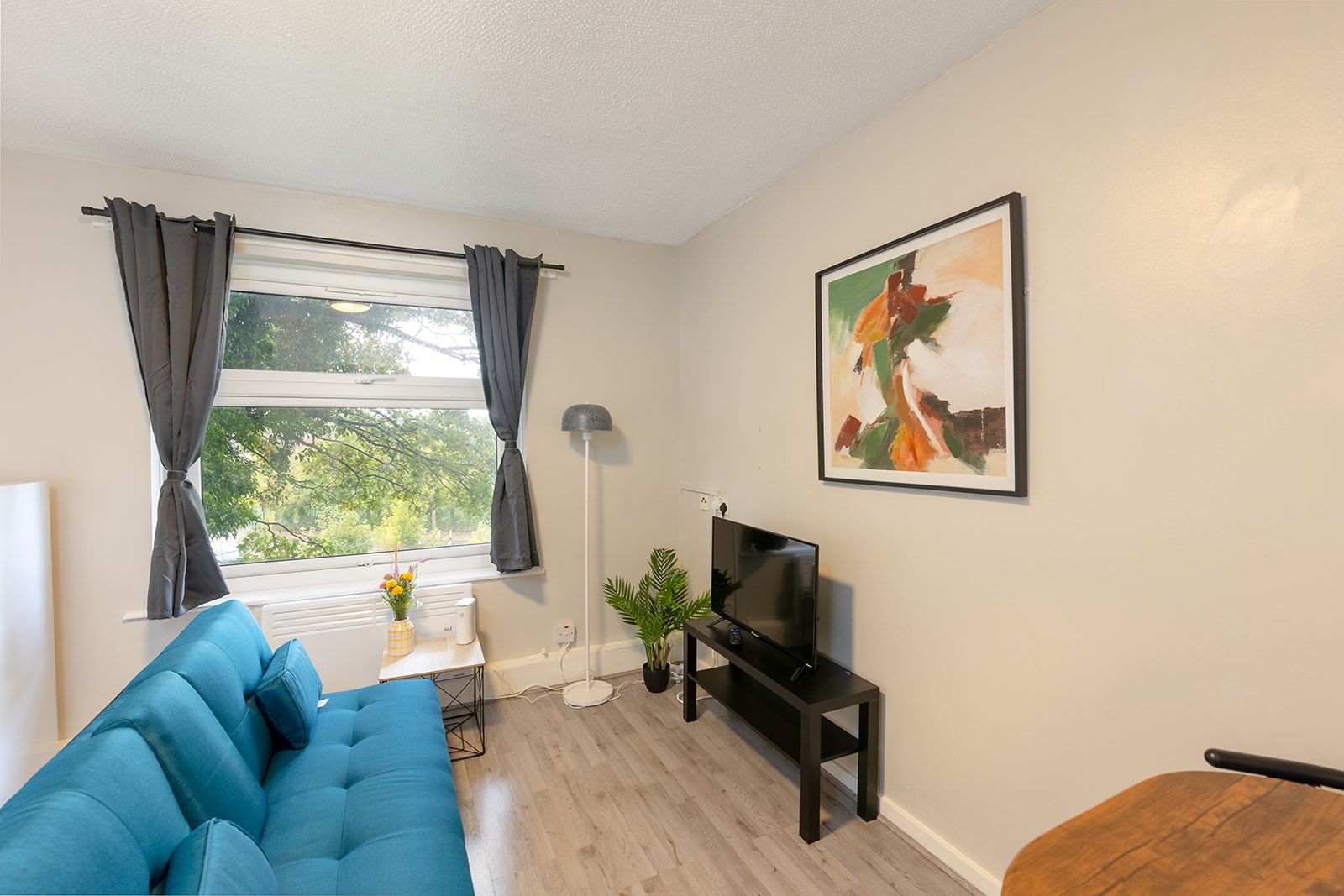 A living room with a blue sofa, a TV on a stand, a plant, and a painting on the wall.