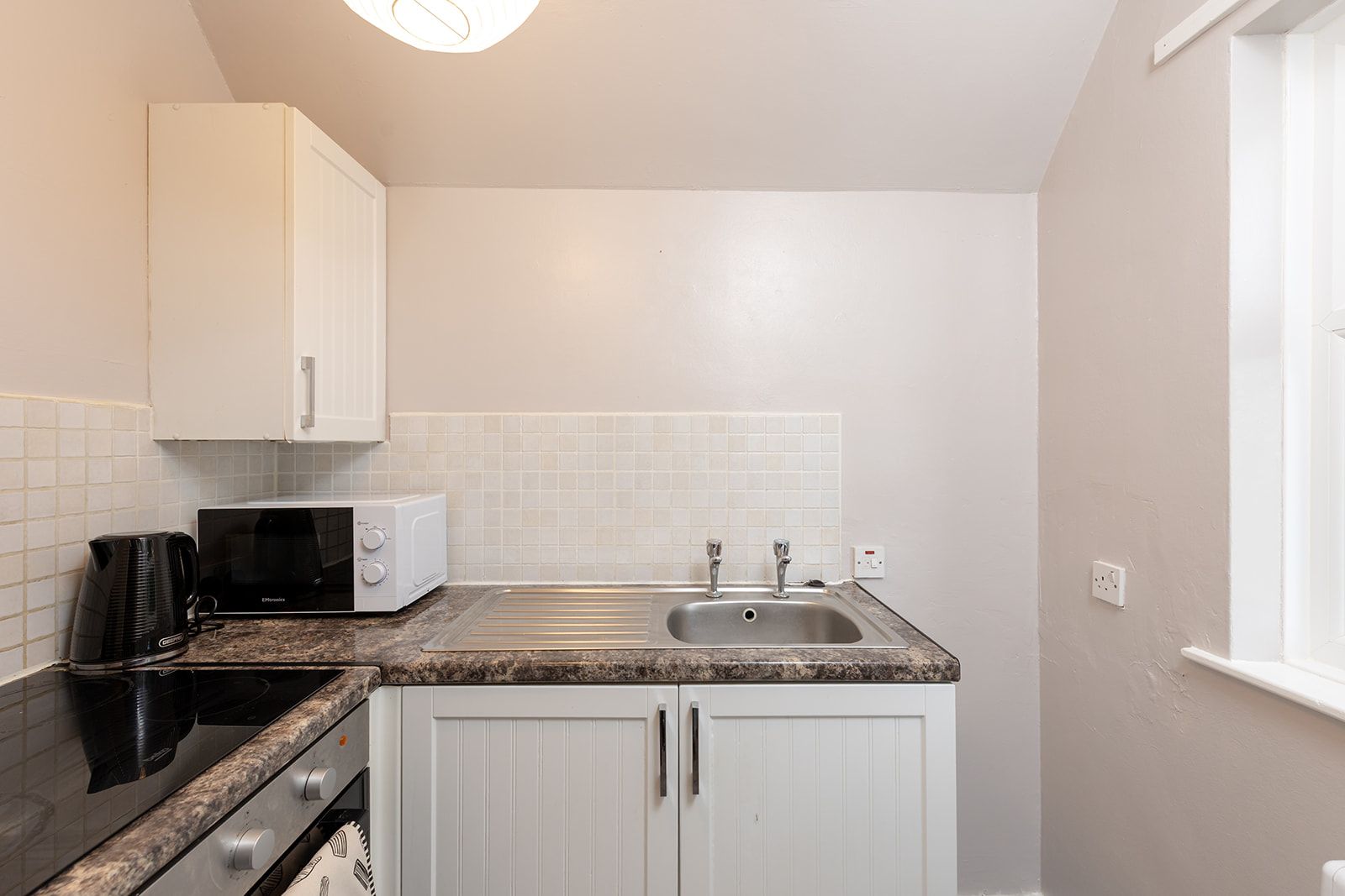 A compact kitchen with white cabinets, a microwave, a coffee maker, and a sink.