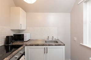 A compact kitchen with white cabinets, a microwave, a coffee maker, and a sink. - 1BR Flat in Stockton | Cozy | Near Station (Stockton-on-Tees)