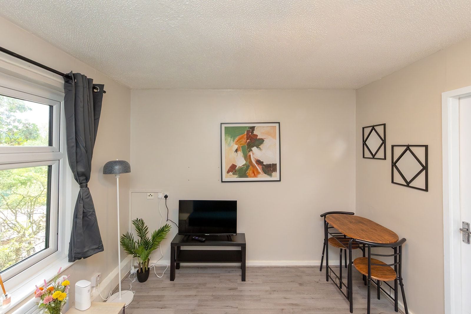 Ein Zimmer mit Fernseher, einem Esstisch mit Stühlen, einer Zimmerpflanze und Bildern an der Wand.