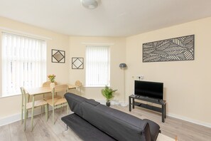 Un salon comprenant un canapé, une table à manger avec des chaises, un téléviseur posé sur un meuble et une lampe sur pied.