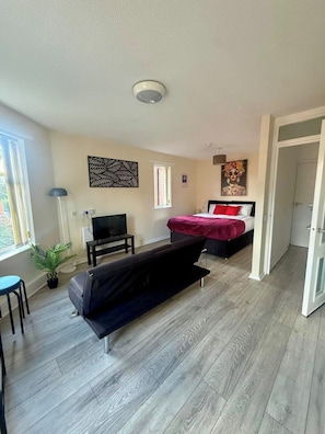 A modern room with a bed, a sofa, a TV, and a window. - 1BR Flat w/ King sized beds | Near Station (Stockton-on-Tees)
