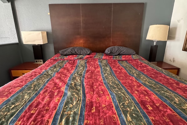 Ein Bett mit einem gemusterten Überwurf, zwei Kissen, einem Holzkopfende und Nachttischlampen.