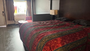 Ein Hotelzimmer mit einem großen Bett, einem roten Sessel, einem Fenster mit Vorhängen und einer Wandlampe.