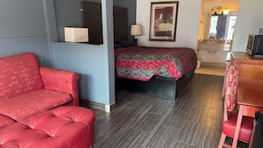 Ein Zimmer mit einem roten Sofa, einem Bett mit einem gemusterten Überwurf, einem Holzkleiderschrank und einem Spiegel.