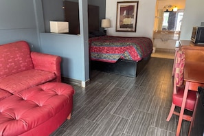 Ein Zimmer mit einem roten Sofa, einem Bett mit einem gemusterten Überwurf, einem Holzkleiderschrank und einem Spiegel.