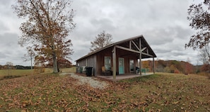 Une cabane rustique dotée d’un porche, entourée d’une zone herbeuse parsemée de feuilles.