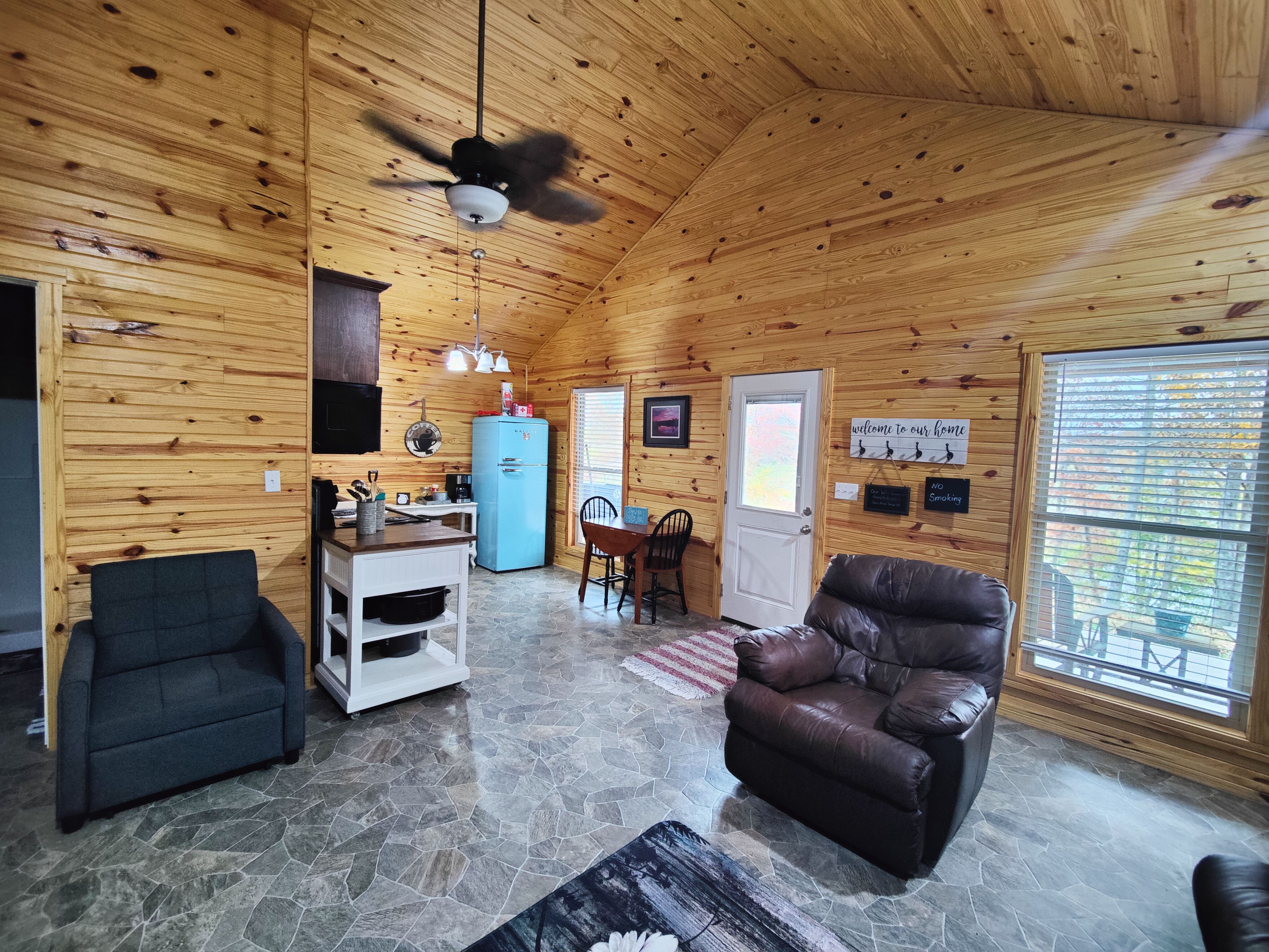 L’intérieur d’un chalet accueillant, avec un sol en pierre, des murs en bois, un réfrigérateur bleu, un canapé en cuir et un coin repas.