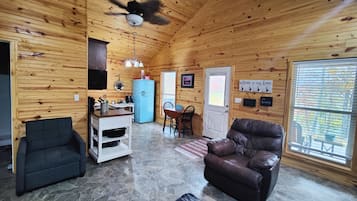 Een gezellig chalet interieur met een stenen vloer, houten wanden, een blauwe koelkast, een leren bank en een eethoek.